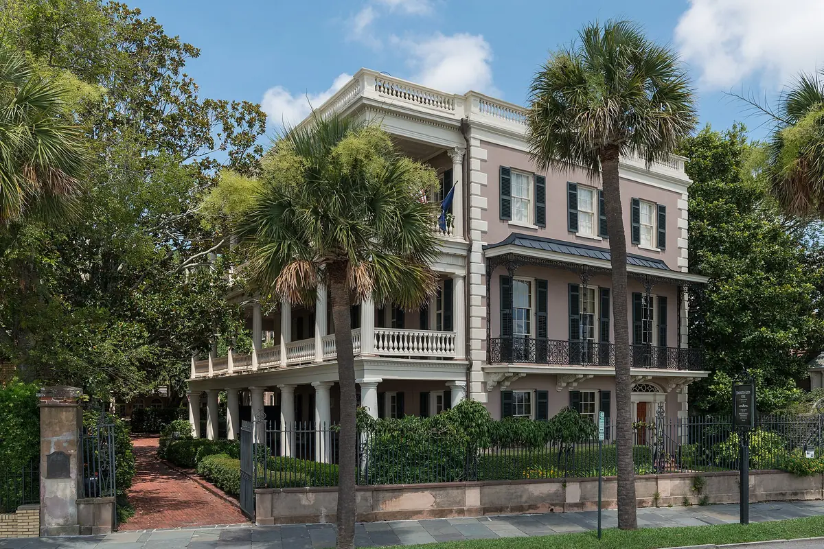 Ein blassrosa Antebellum-Haus mit Säulenarkaden und einer Balustrade an der East Battery, hinter einem schmiedeeisernen Zaun und eingerahmt von Palmetto-Palmen